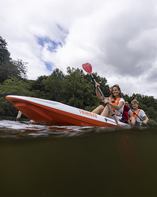 Family enjoying a river trek in a bright orange TAHE kayak amidst a vibrant verdant forest.