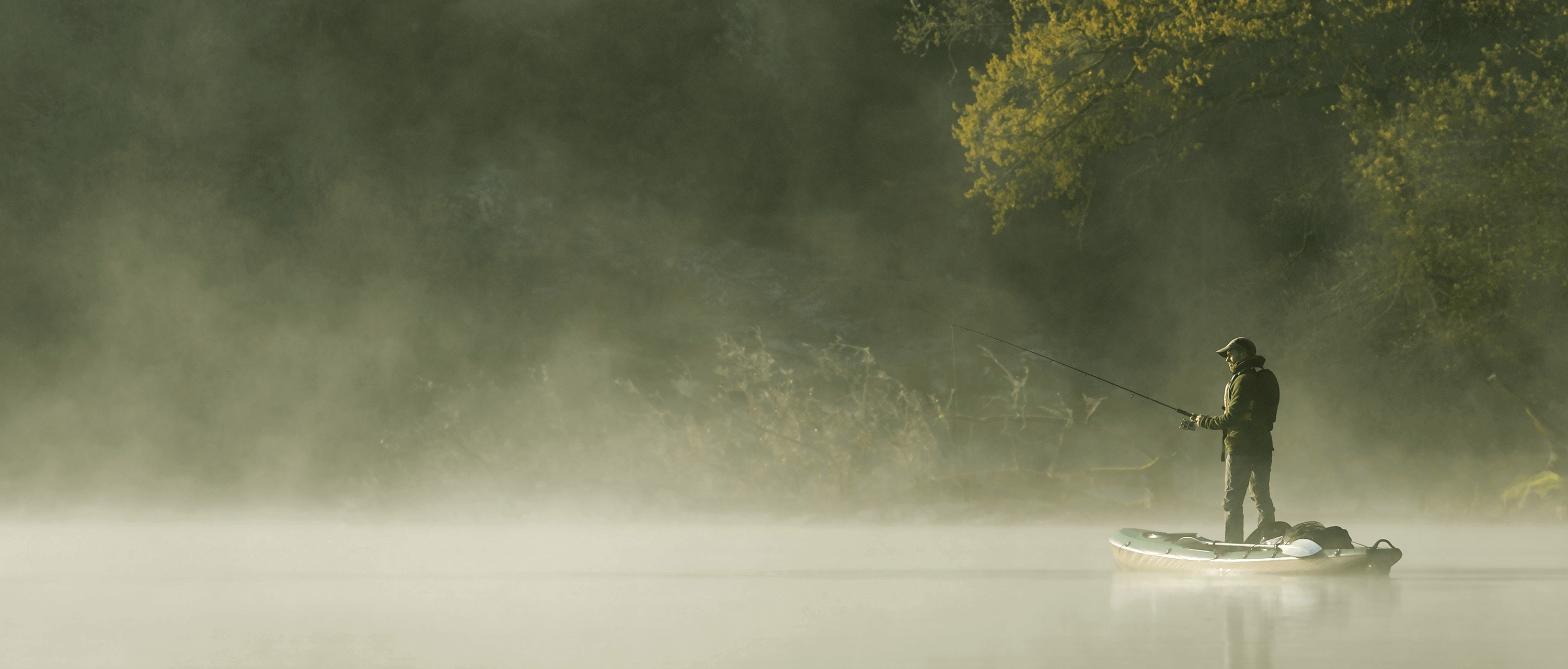 Angler standing steady on a TAHE fishing kayak, casting a line into the morning mist on a calm river.
