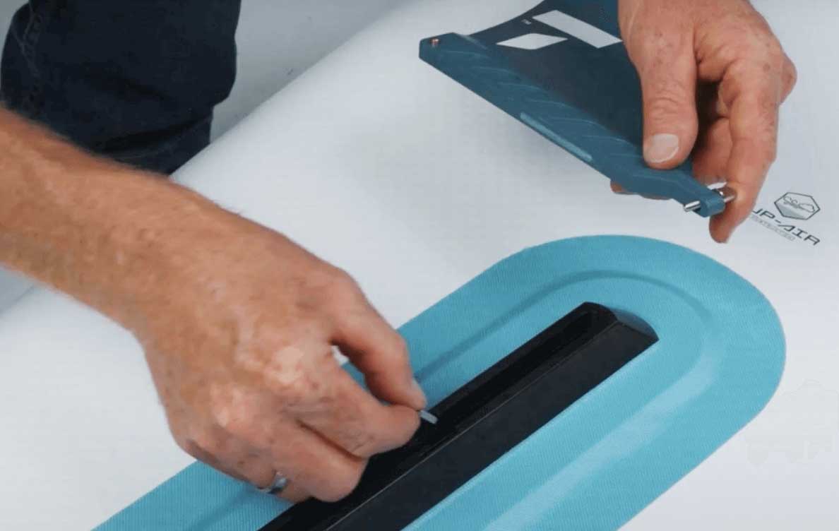 Close-up of a paddler installing a removable fin on a TAHE SUP board.