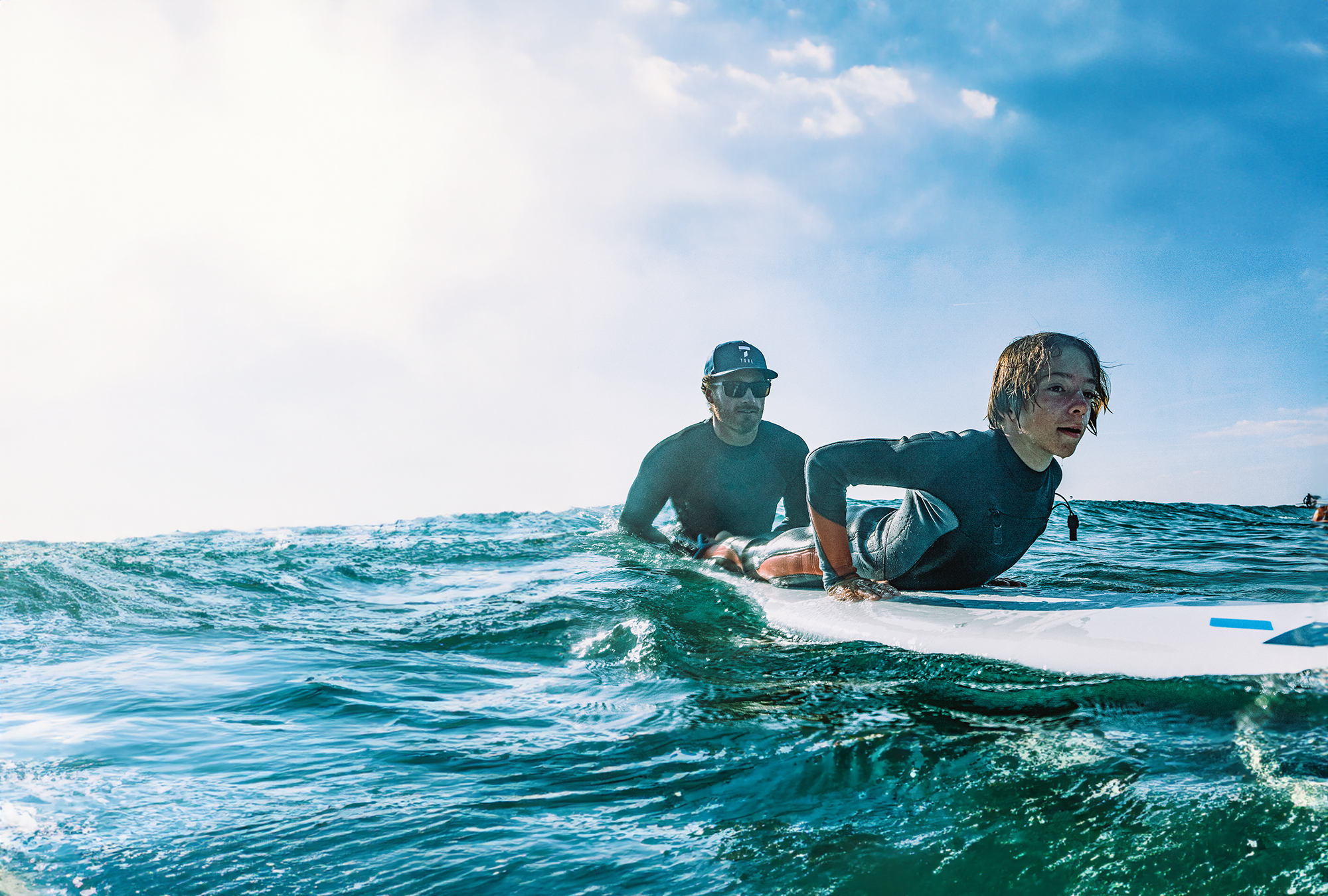 A surf instructor guiding a young student on a TAHE softboard during a lesson in the surf.