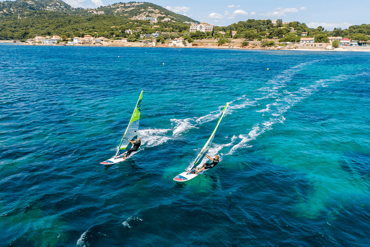 Aerial view of two TAHE windsurfers with green sails navigating on blue sea.